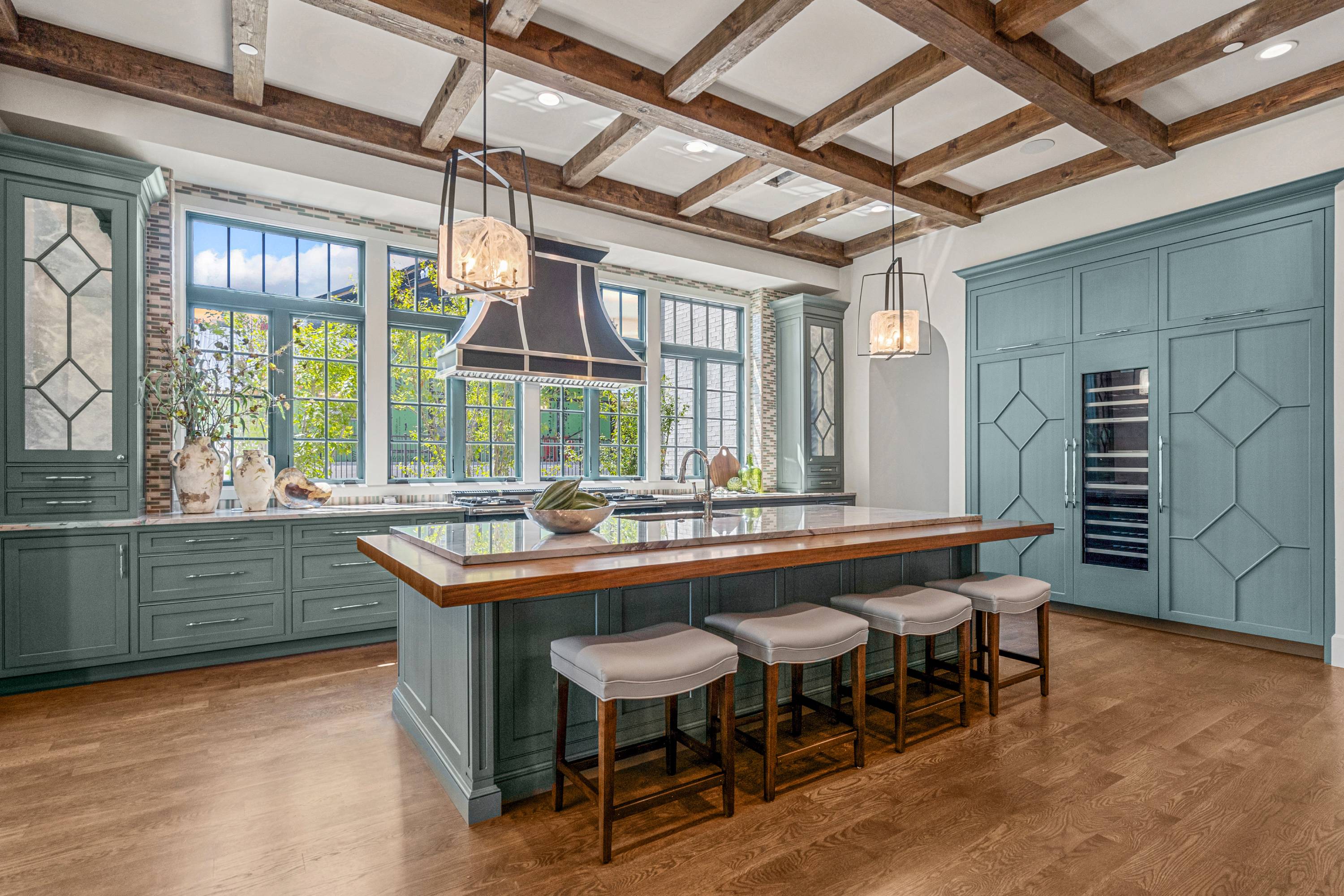 An English Arts and Crafts inspired kitchen featuring cadet blue cabinetry, a large central island with seating, and a high ceiling with exposed wooden beams.